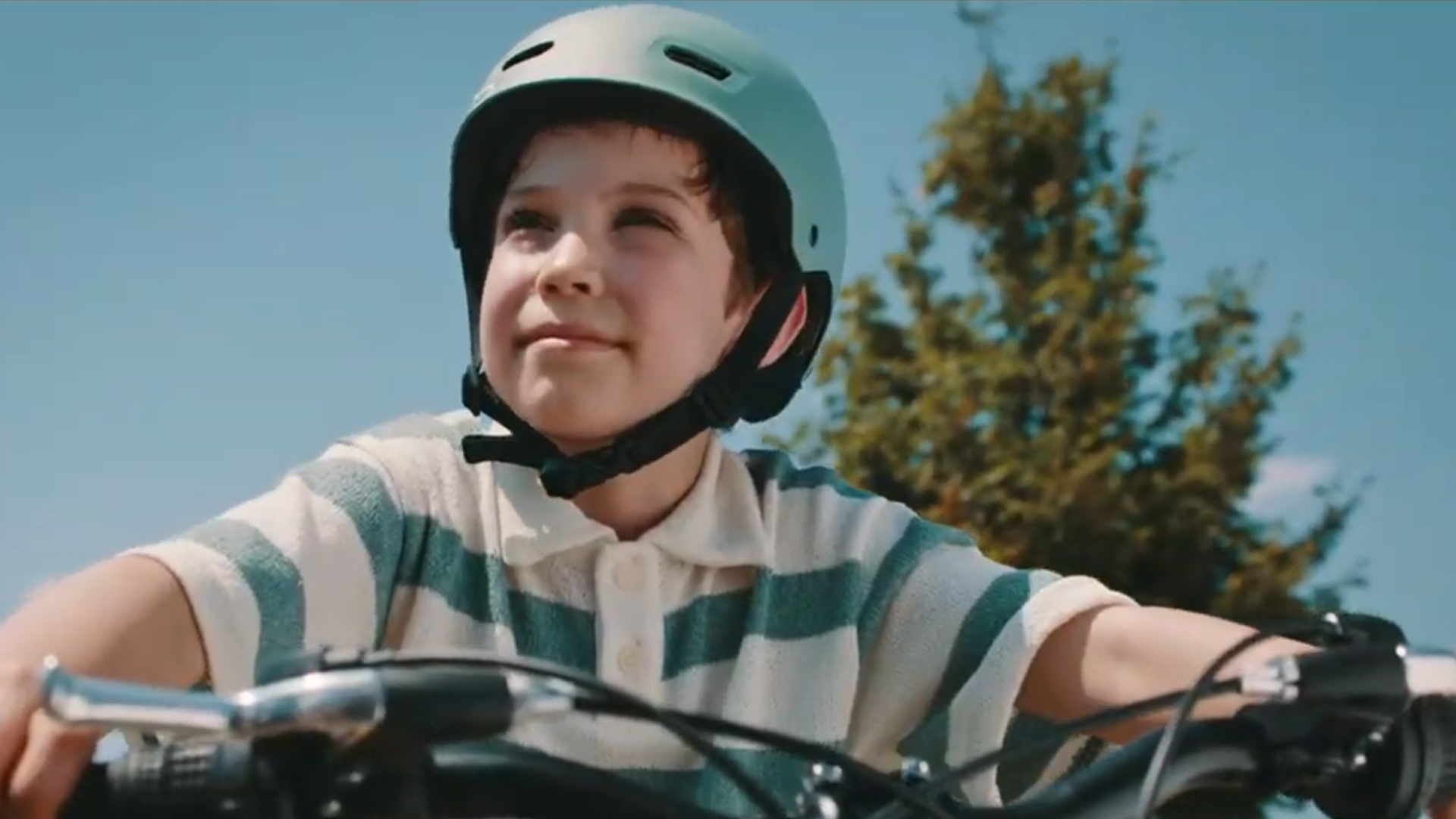 Un copil cu cască pe bicicletă, în aer liber.