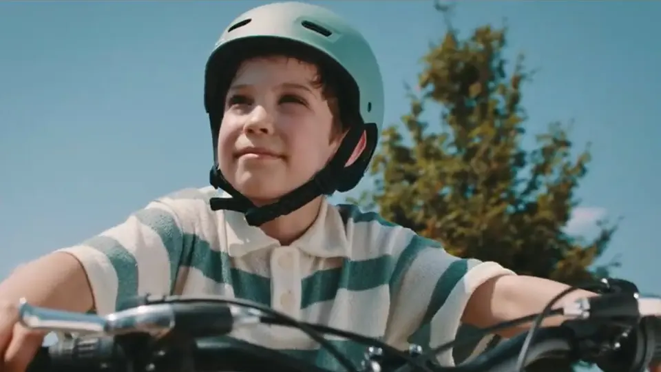 Un copil cu cască pe bicicletă, în aer liber.