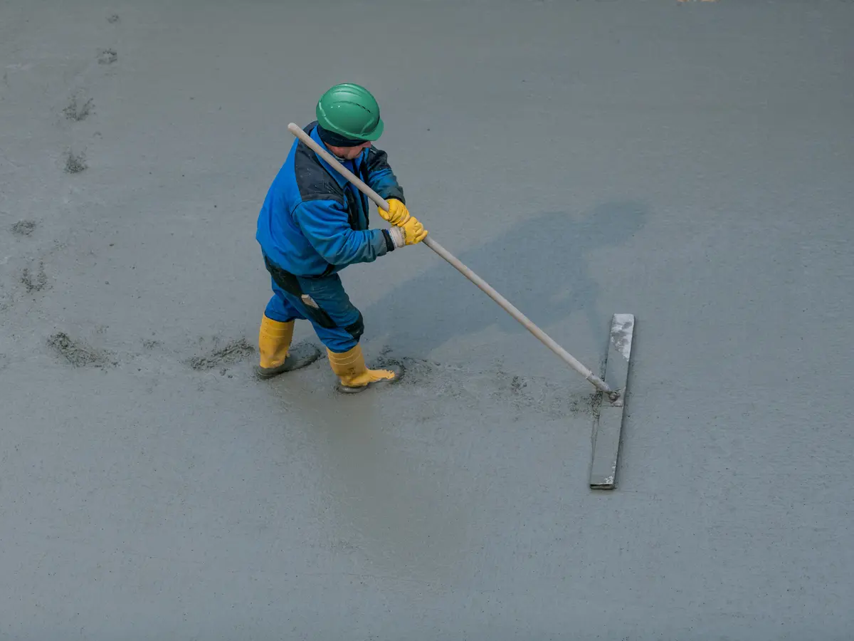 Muncitor ajustând suprafața betonului proaspăt turnat pe un șantier de construcții.